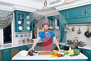 Guy in apron and hat in the kitchen made salad for vegans with lettuce and zucchini. Handsome man at home kitchen concept