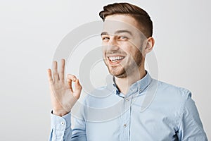 Guy assuring coworker work be done in time. Pleased good-looking young male in blue shirt showing okay or excellent