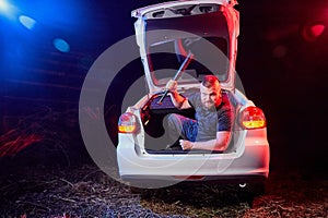 Guy with an axe in the trunk of a car in a night time