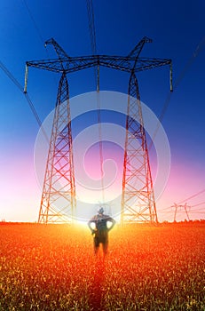 Guy on the background of high-voltage power lines at sunset. green field