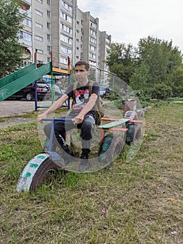 A guy with a backpack sits on a toy bike