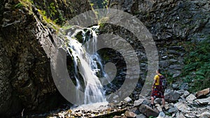 A guy with a backpack is standing near a waterfall