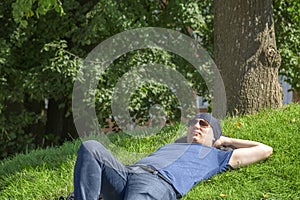 A guy in a bandana and sunglasses is napping on a green lawn on a sunny summer day