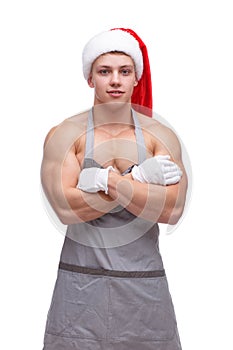 A guy with a bare chest is in a kitchen apron and a Santa hat standing with his arms crossed over his chest. Isolated.