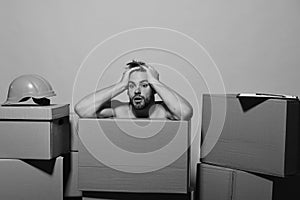 Guy with bare shoulders holds head among boxes .