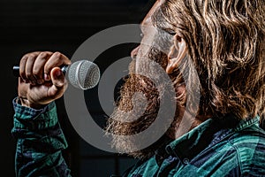 Guy with beard singing in microphone. Bearded man wearing checkered shirt. Male karaoke singer. Bearded man singing with