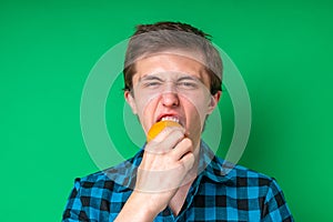 Guy bites sour unripe citrus. man makes a face because sour taste of fruit