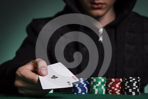 A guy in a black jacket holds a pair of aces against a pile of p