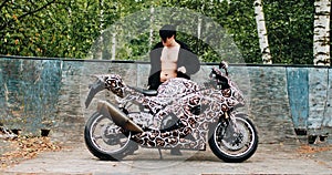 A guy in a black jacket posing next to a sports bike.