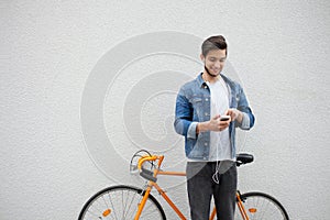 The guy in a blue denim jacket standing on wall background. young man near orange bicycle. Smiling student with bag