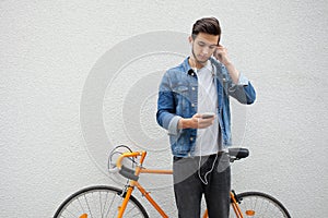 The guy in a blue denim jacket standing on wall background. young man near orange bicycle. Smiling student with bag