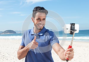 Guy with blue shirt and beard at beach taking selfie with stick