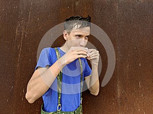 A guy in a blue t-shirt drinks a cup of coffee on a background of a rusty steel wall
