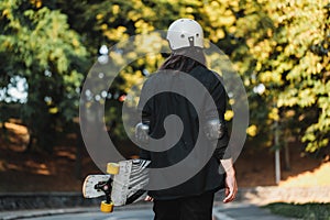 The guy with the board walks down the street. Longboarding at sunset.