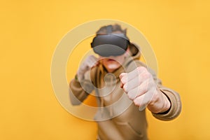Guy boxing on yellow background with VR helmet on his head. Isolated. Close-up and Focus on the fist. Young man playing VR games.