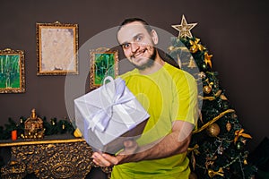 A guy in a bright green T-shirt holds a gift box in his hands and wants to give it. The man is happy with the new year. Christmas