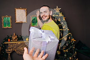 A guy in a bright green T-shirt holds a gift box in his hands and wants to give it. The man is happy with the new year. Christmas