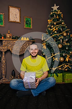 A guy in a bright green T-shirt holds a gift box in his hands and wants to open a surprise. The man is happy about the new year