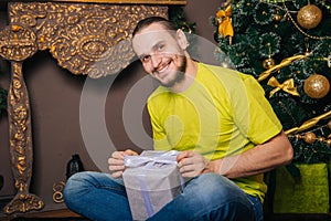 A guy in a bright green T-shirt holds a gift box in his hands and wants to open a surprise. The man is happy about the new year