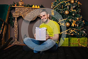 A guy in a bright green T-shirt holds a gift box in his hands and wants to open a surprise. The man is happy about the new year