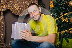 A guy in a bright green T-shirt holds a gift box in his hands and wants to open a surprise. The man is happy about the new year