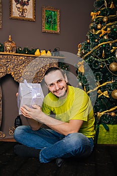 A guy in a bright green T-shirt holds a gift box in his hands and wants to open a surprise. The man is happy about the new year