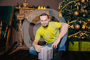 A guy in a bright green T-shirt holds a gift box in his hands and wants to open a surprise. The man is happy about the new year