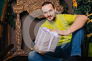 A guy in a bright green T-shirt holds a gift box in his hands and wants to open a surprise. The man is happy about the new year