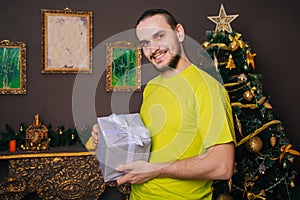 A guy in a bright green T-shirt holds a gift box in his hands and wants to open a surprise. The man is happy about the new year