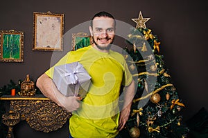 A guy in a bright green T-shirt holds a gift box in his hands and wants to open a surprise. The man is happy about the new year