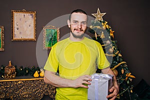 A guy in a bright green T-shirt holds a gift box in his hands and wants to open a surprise. The man is happy about the new year