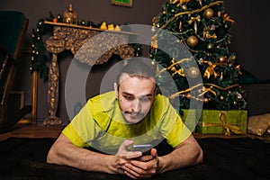 A guy in a bright green T-shirt is lying on the carpet with a mobile phone in his hands. Communicate on a smartphone against the