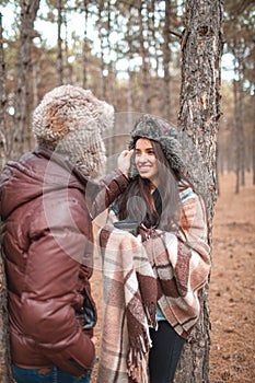 The guy carefully adjusts the fur hat on the girl`s head, the girl smiles coyly. Outdoors.