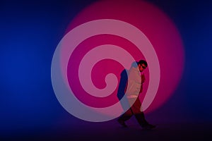 Guy in casual clothes dancing hip hop elements in studio with blue light. Dancer is in red circle of spotlight and