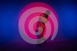 Guy in casual clothes dancing hip hop elements in studio with blue light. Dancer is in red circle of spotlight and