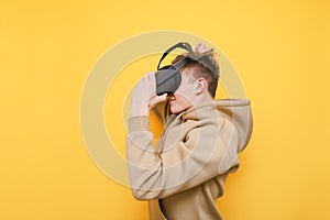 Guy in casual clothes wears a VR helmet and is about to play video games isolated on a yellow background. Young man testing a