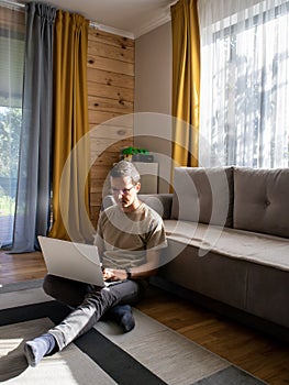 A guy in casual clothes is working on the floor in a sunny loft apartment