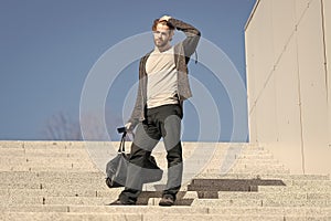 Guy in casual wear stand on stairs on blue sky, fashion. Man with bag, smartphone on steps on sunny outdoor. Macho ready