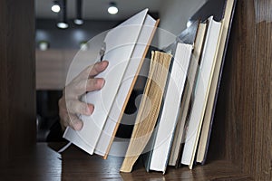 The guy chooses a book to read from the shelf. Hand of male selecting a book from bookshelf