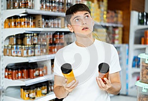 Guy choosing natural aromatic spices in glass jars in grocery store