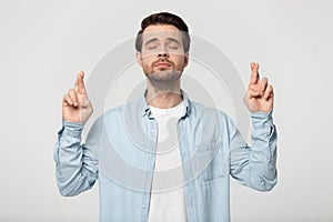 Guy with closed eyes crossing fingers posing isolated on grey