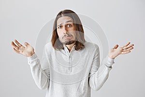 Guy is confused with questions. Studio shot of handsome funny man with beard and long hair making weird face and