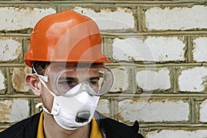 the guy is a construction worker in a protective construction helmet a respirator and protective glasses against the