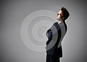 Guy with cool hairstyle, in black suit on naked body. He raised his hands and posing sideways on gray background. Close up