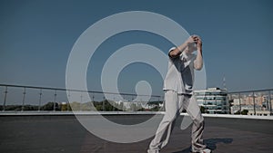 The guy coolly dances breakdance on the roof of the house. A man dances an energetic athletic dance.