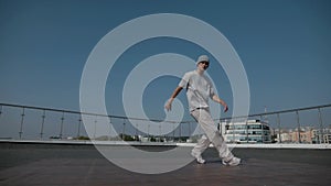 The guy coolly dances breakdance on the roof of the house. A man dances an energetic athletic dance.