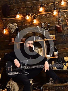 Guy in cozy warm atmosphere play relaxing soul music. Favourite activity. Man with beard holds black electric guitar