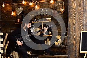 Guy in cozy warm atmosphere play relaxing soul music. Man bearded musician enjoy evening with bass guitar, wooden