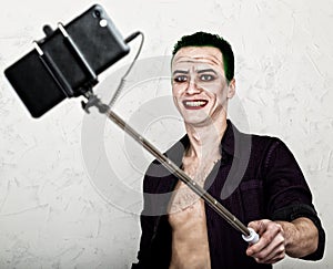 Guy with crazy joker face, green hair and idiotic smile. carnaval costume. making selfy photo