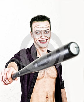 Guy with crazy joker face holding baseball bat, green hair and idiotic smike. carnaval costume